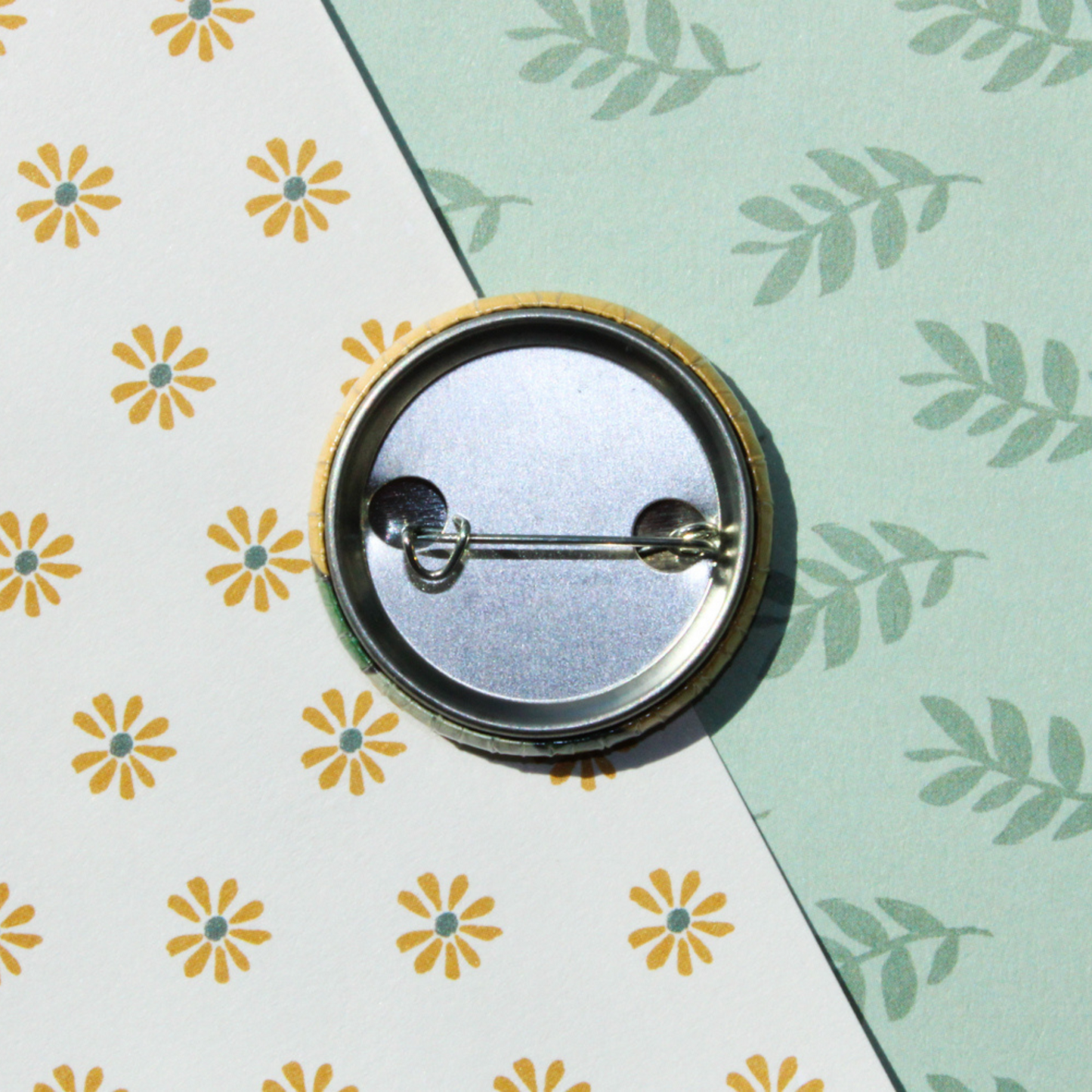 A leaf and flower patterned background with the back of a circle pin on top with it's clasp.