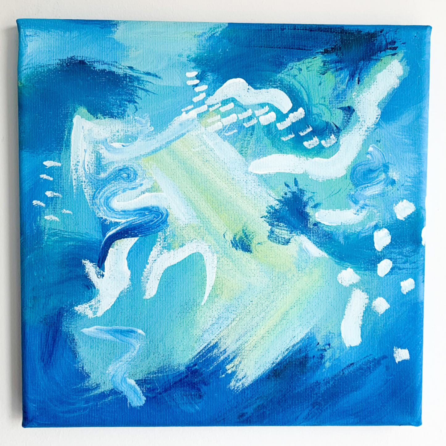 An abstract blue painting is pictured in a black frame on a grey wall with accents of white and yellow