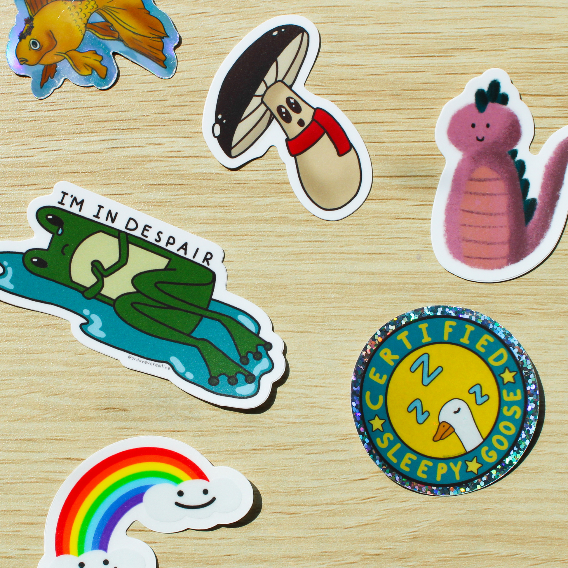 A brown wood background with a goldfish, mushroom, dinosaur, frog, goose, and rainbow sticker scattered across it.