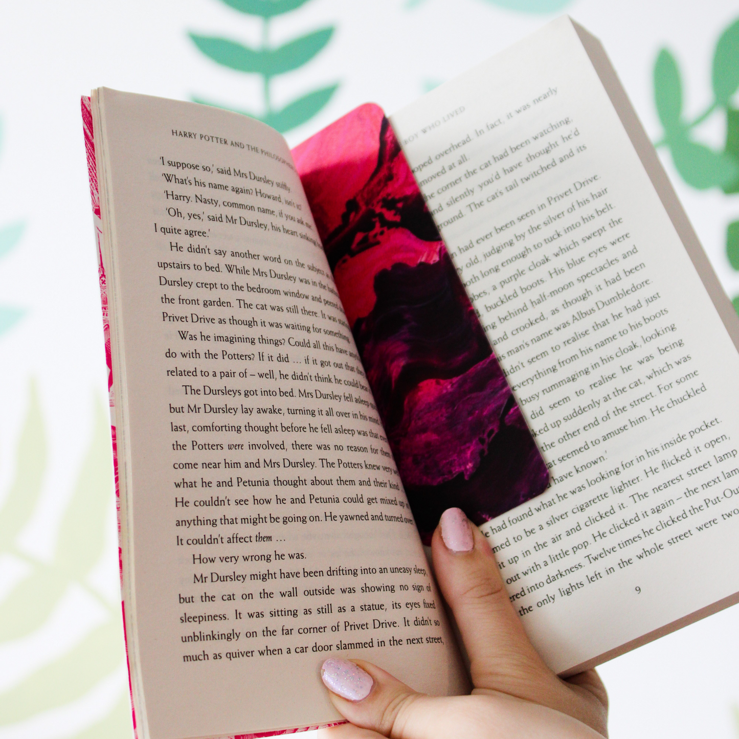 The pink and purple sky bookmark is inside a book being held.