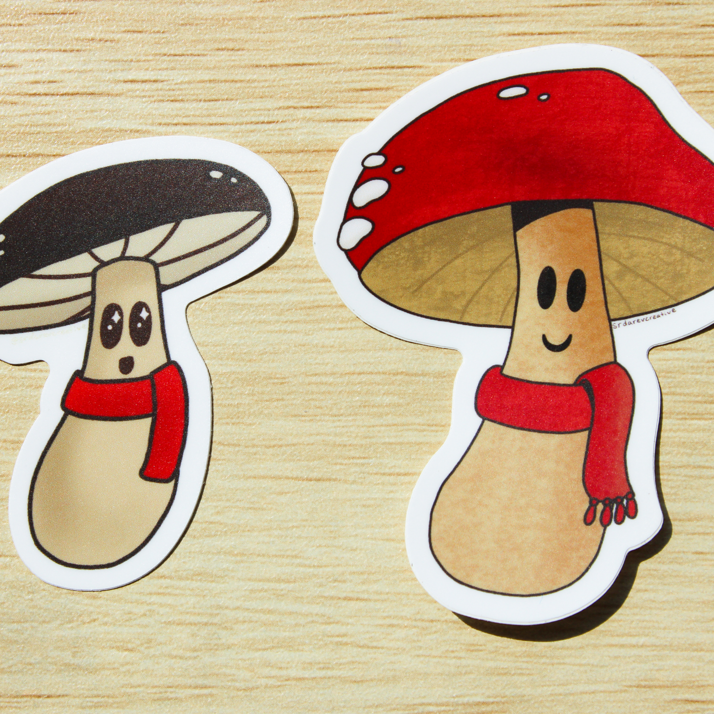 A brown wooden background. On top are two smiling mushroom stickers. On the left is a brown mushroom with a red scarf and on the right is a red mushroom with a red scarf.