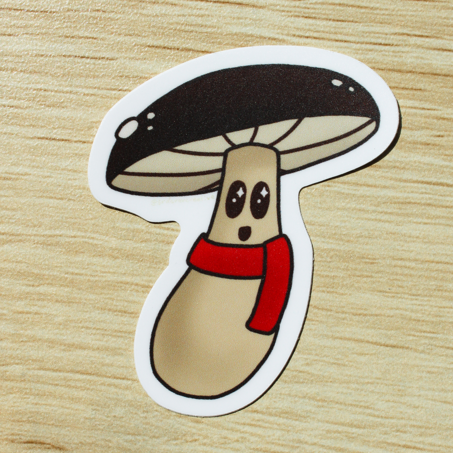 A brown wooden background. On top is a brown mushroom sticker with a red scarf and smiling face.