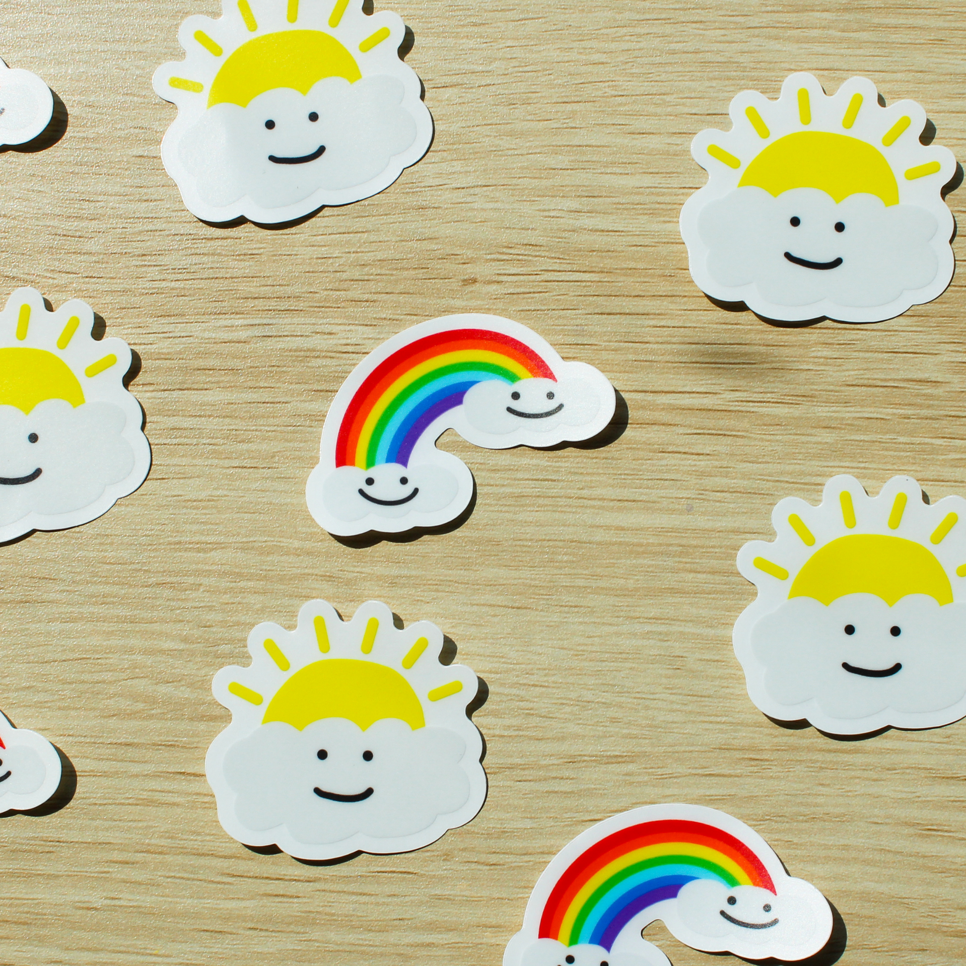 A wooden background with alternating smiling rainbow and smiling sunny cloud stickers.