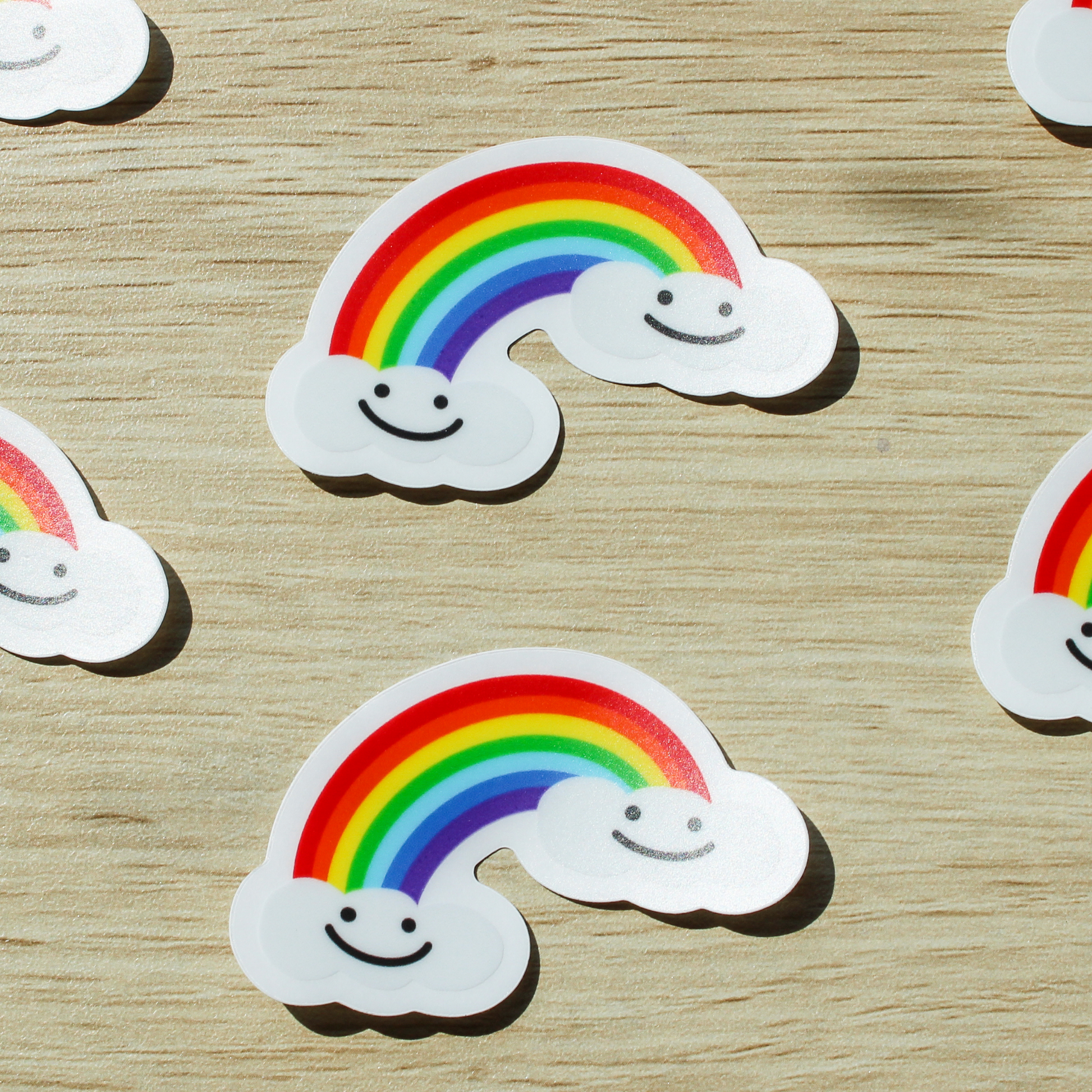 A wooden background with several smiling rainbow cloud stickers.