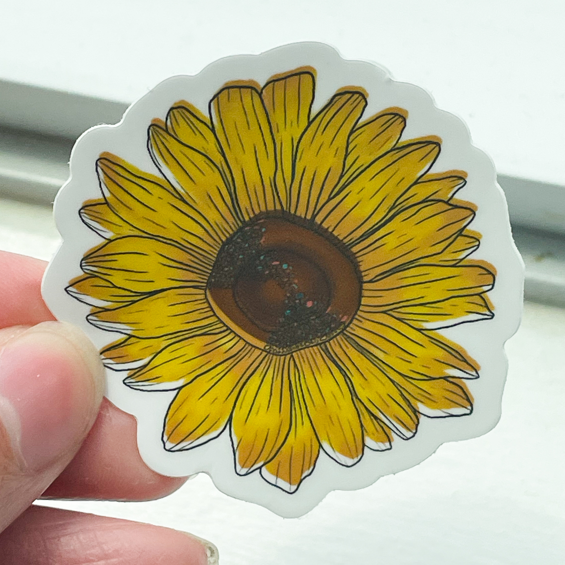 A hand holding a close up of a yellow sunflower sticker