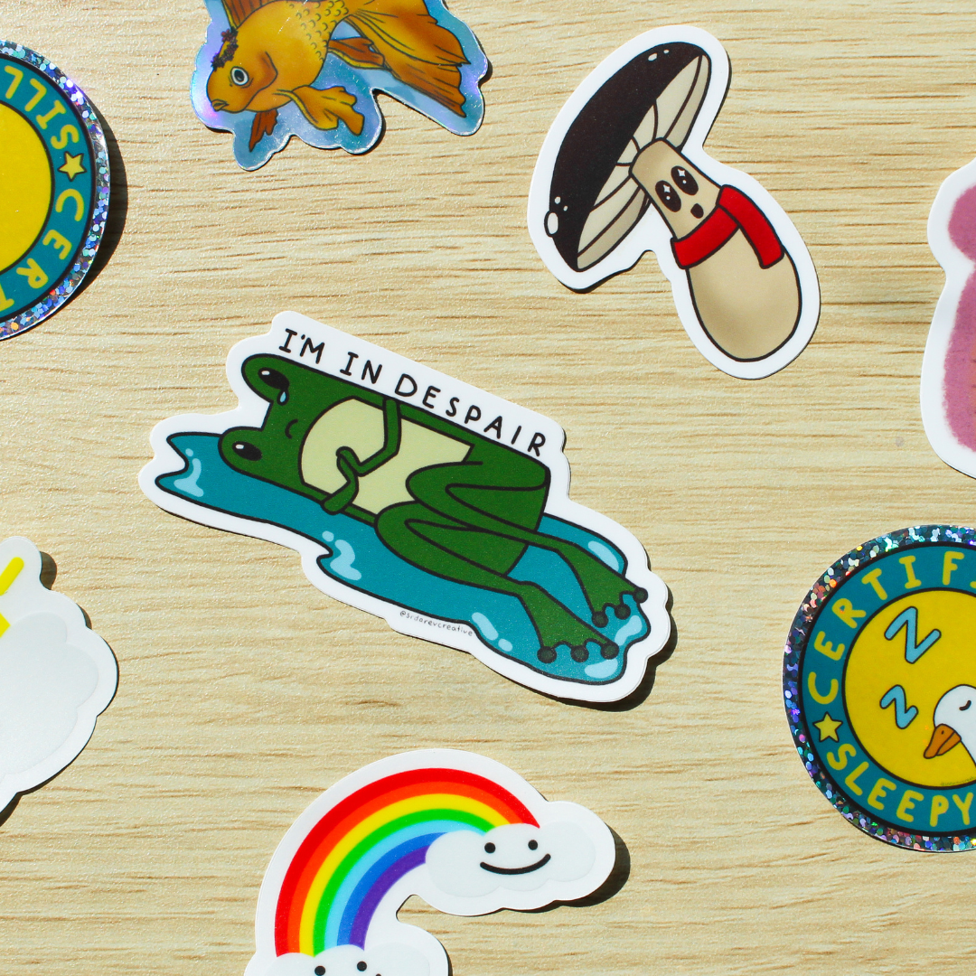 Image of stickers of frog in a puddle crying, rainbow clouds, and silly goose on a light wooden background