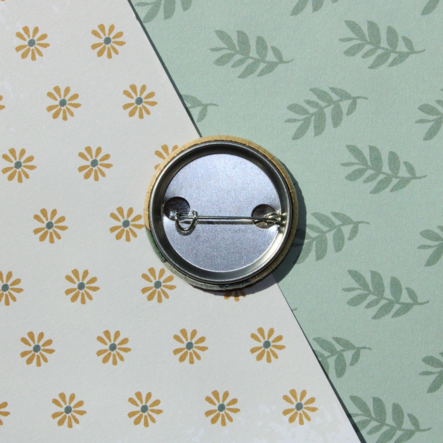 A leaf and flower patterned background with the back of a circle pin on top with it's clasp.