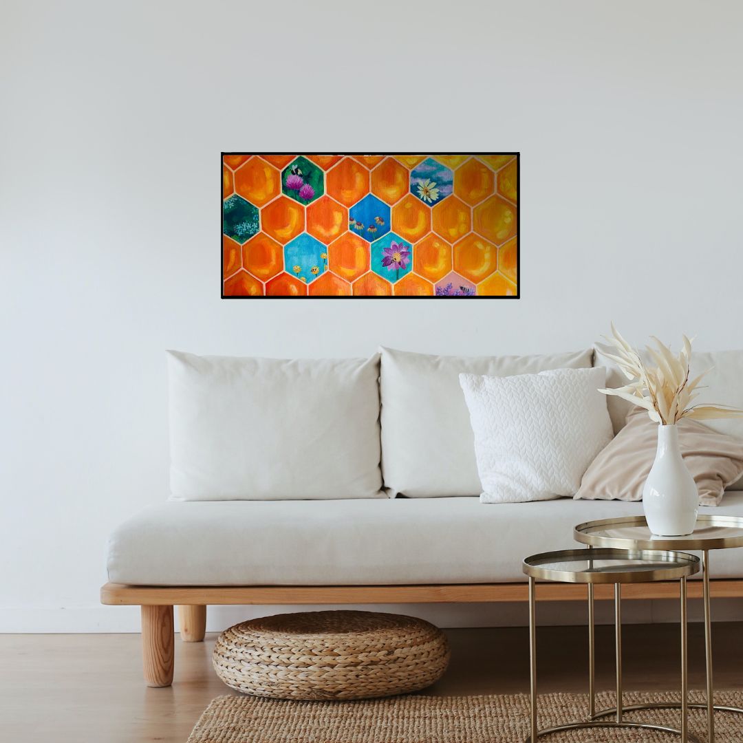 A white couch on a wooden floor with a white wall in the background. On the white wall is an orange honeycomb painting wiht some honeycombs having different colours and flowers and bees painted in them.