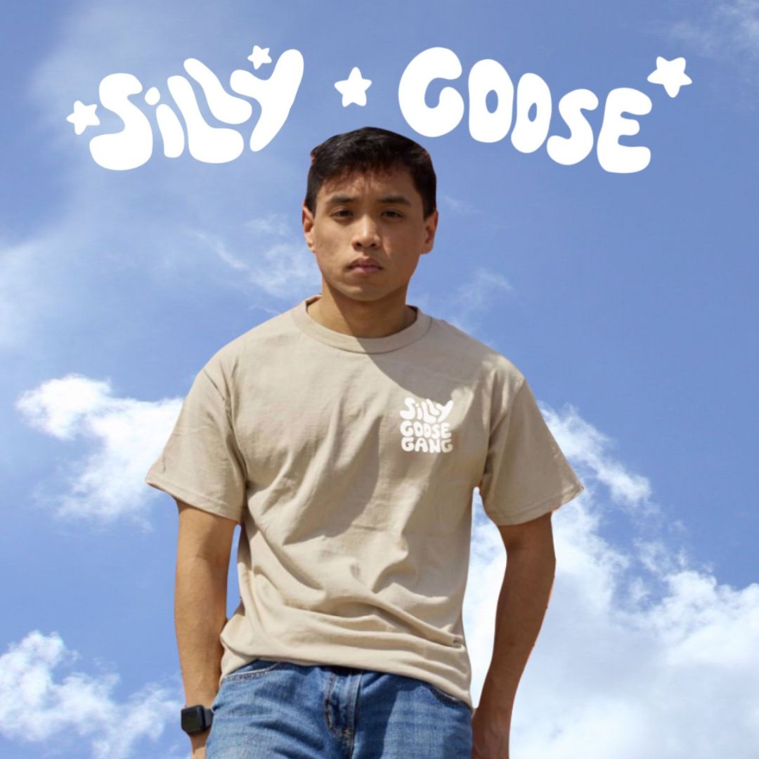 Blue sky background with clouds and "Silly Goose" written on top in white with stars. A man is seen staring ahead in a beige top with "Silly Goose Gang" on the top right. 