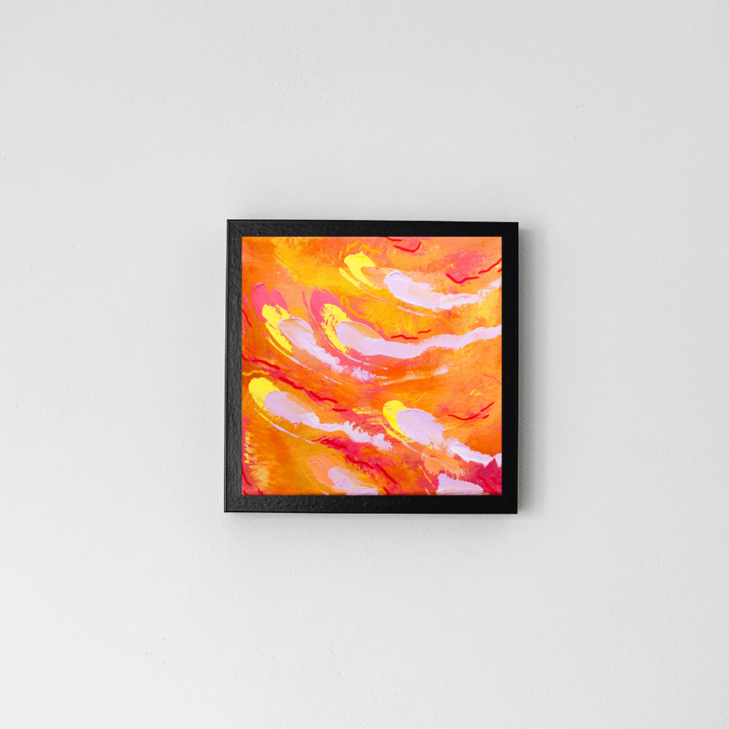 Grey wall with a black frame in the middle. In the black frame is an orange abstract painting with red, yellow, and pale purple streaks throughout.