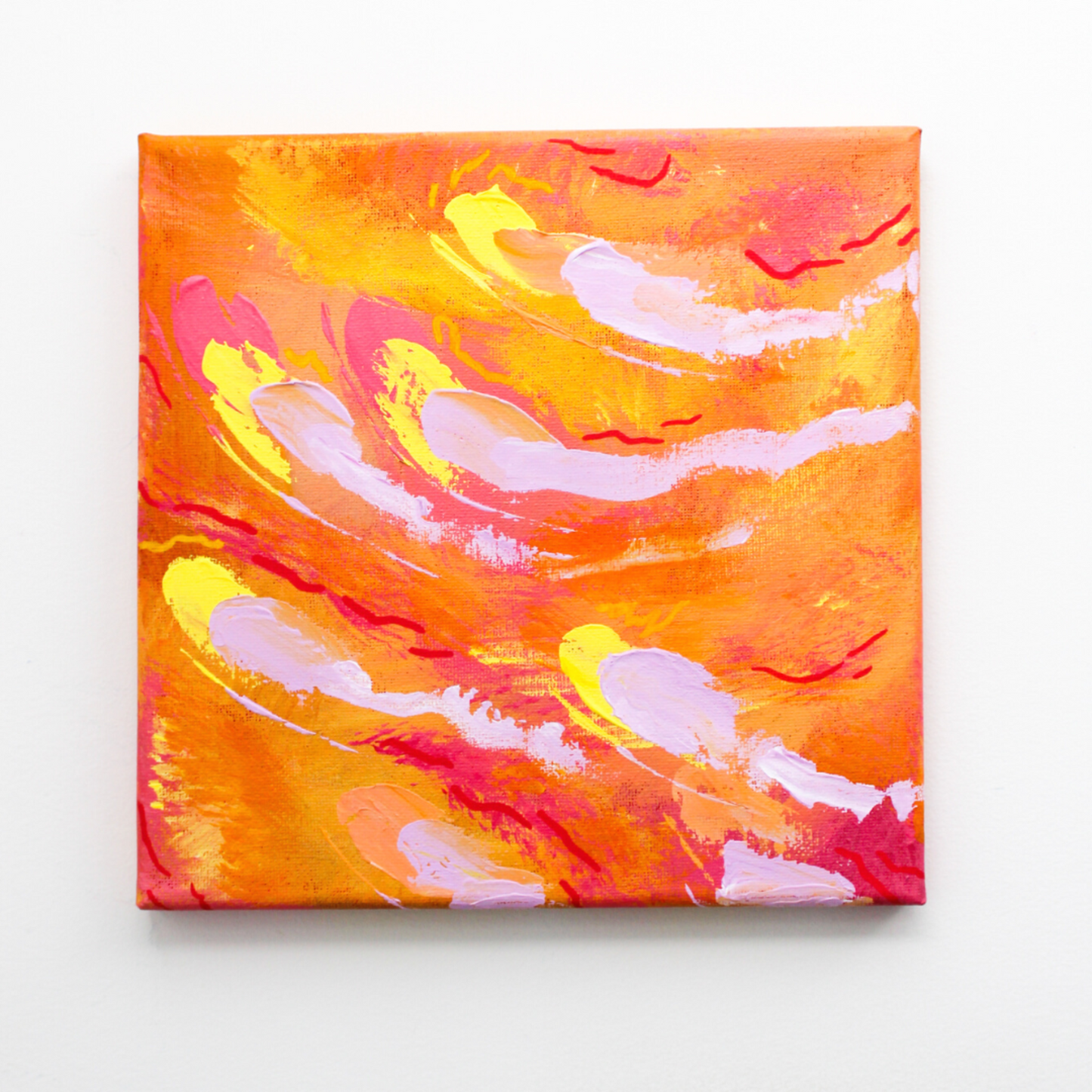 A grey wall and hanging on it is an orange abstract painting with red, yellow, and pale purple streaks throughout.