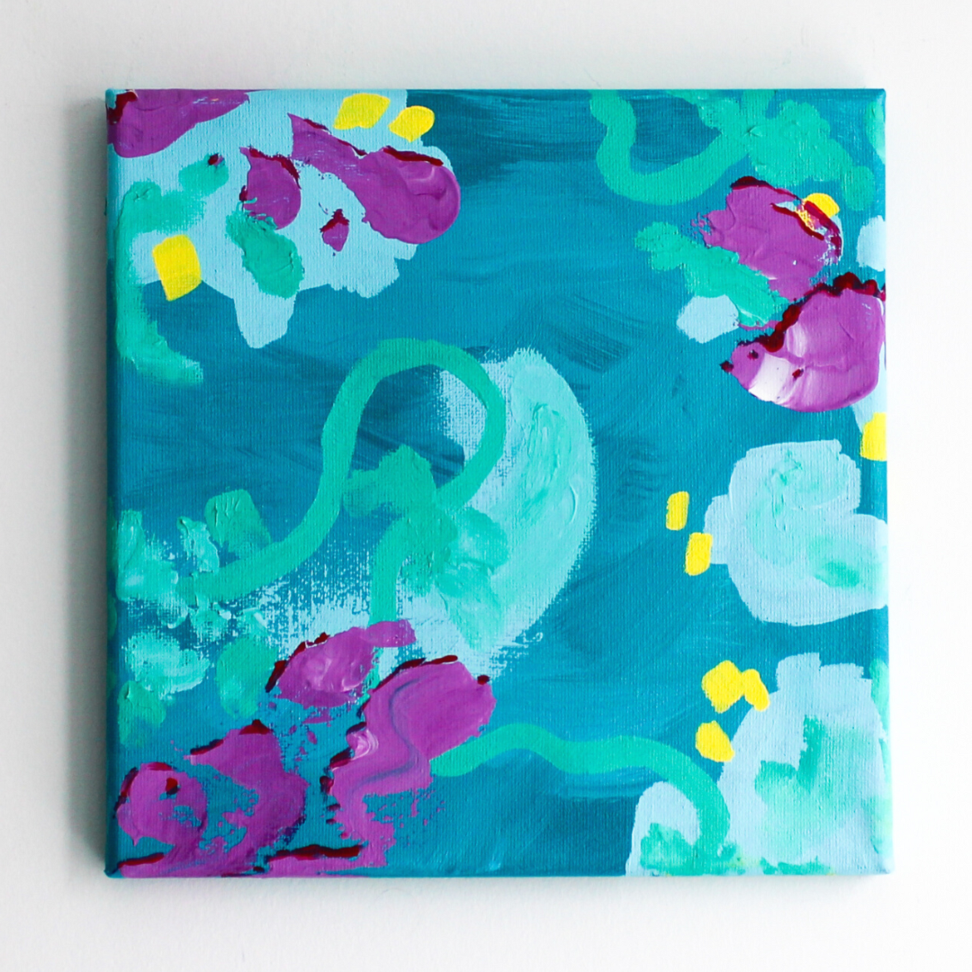 A grey wall with an abstract blue, turquoise, and purple painting.