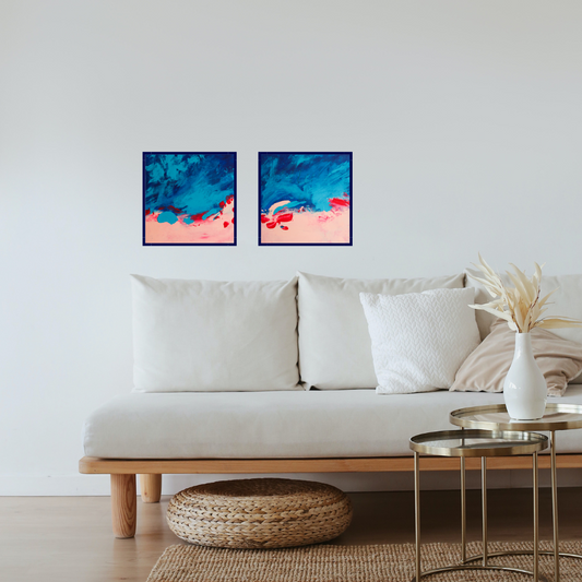 A white couch on a wooden floor with a golden coffee table in the front. Above the couch are two mostly blue abstract square paintings with pink on the bottom blending into the blue with some red swatches.